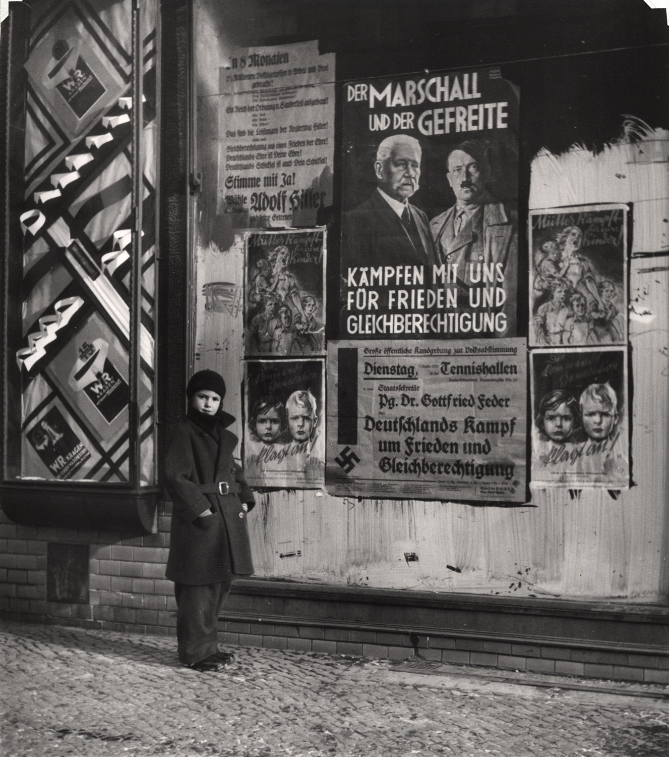 1933. Дочь Вишниака Мара позирует перед избирательным плакатом для Гинденбурга и Гитлера, который гласит «Ммаршал и ефрейтор сражаются вместе с нами за мир и равные права», Вильмерсдорф, Берлин