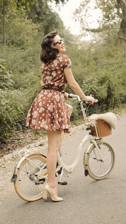 Девушка в коротеньком, коричневом платье с цветочным принтом на велосипеде