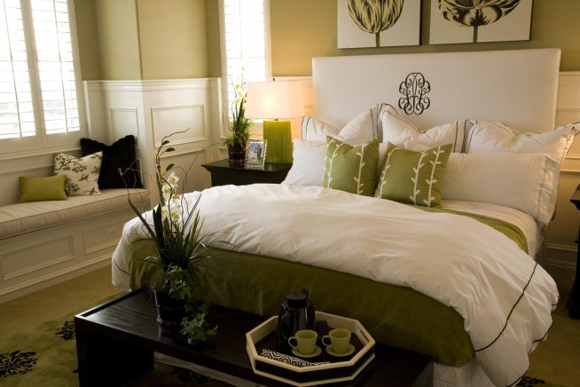 Кровать в спальне с одеялом и подушками белого и зеленого цветов